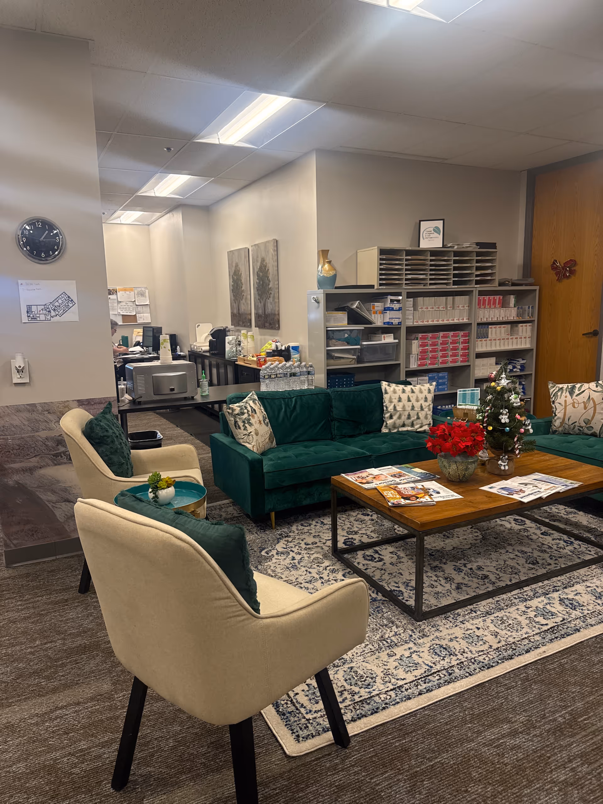 Cozy indoor lounge with green sofa, beige chairs, coffee table, magazines, and shelves.