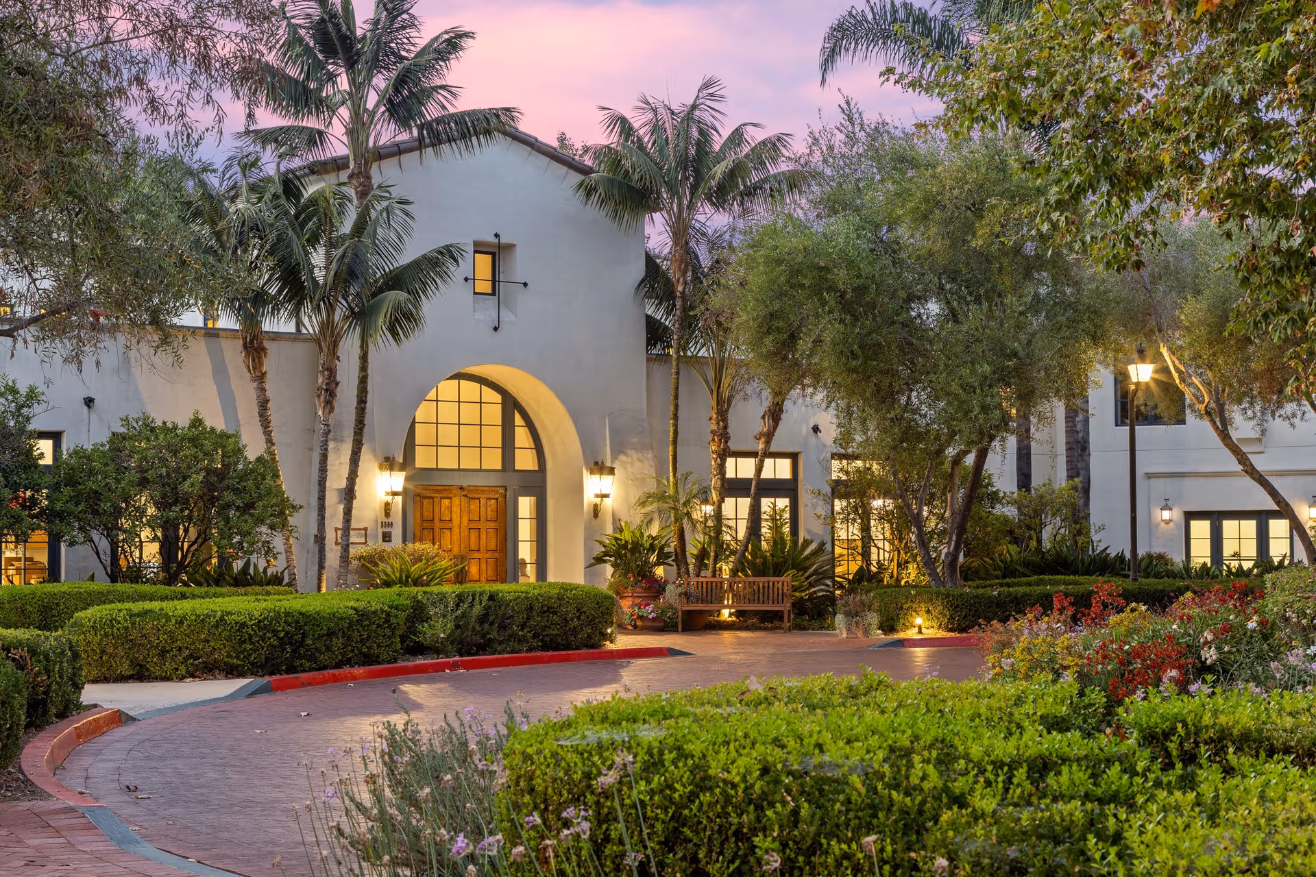 Maravilla senior living facility exterior with arched entry, palm trees, and landscaped grounds at dusk.