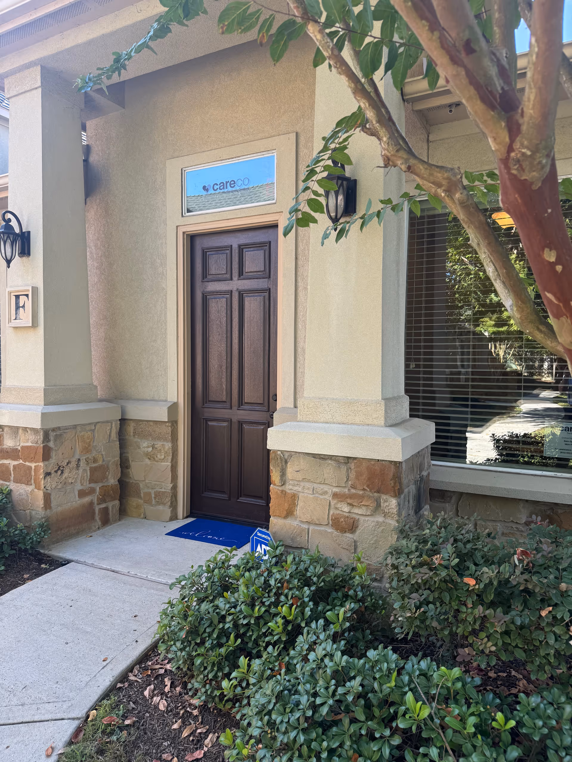 Front entrance of CareCo senior home with brown door and landscaping.