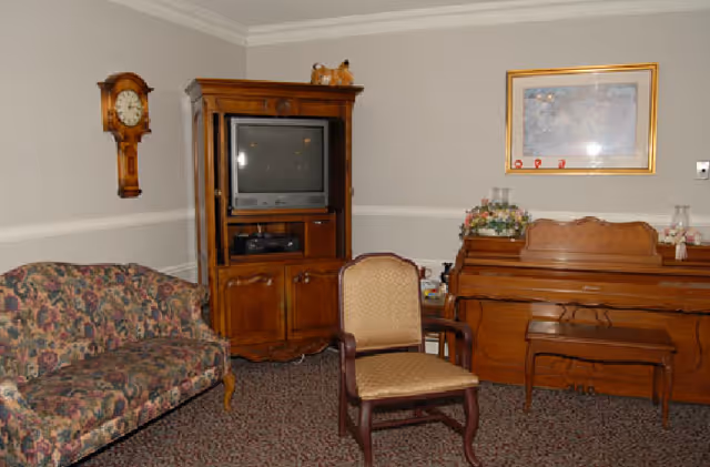 A cozy living room with floral sofa, wooden TV cabinet, piano, and wall clock.