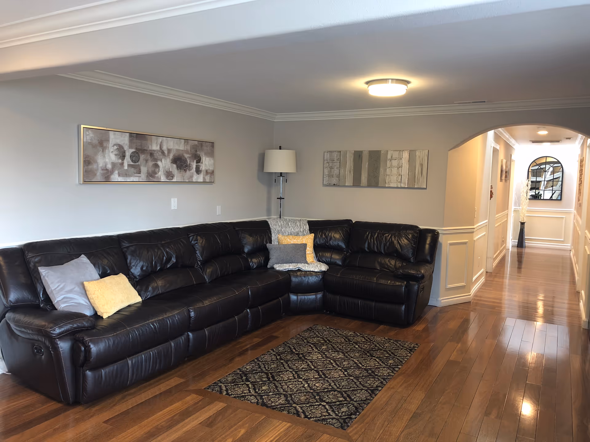 Spacious living room with a black leather sectional, wall art, and hardwood floors.