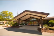 Front entrance of The Village of Ashland senior living facility with a covered drop-off and landscaping.