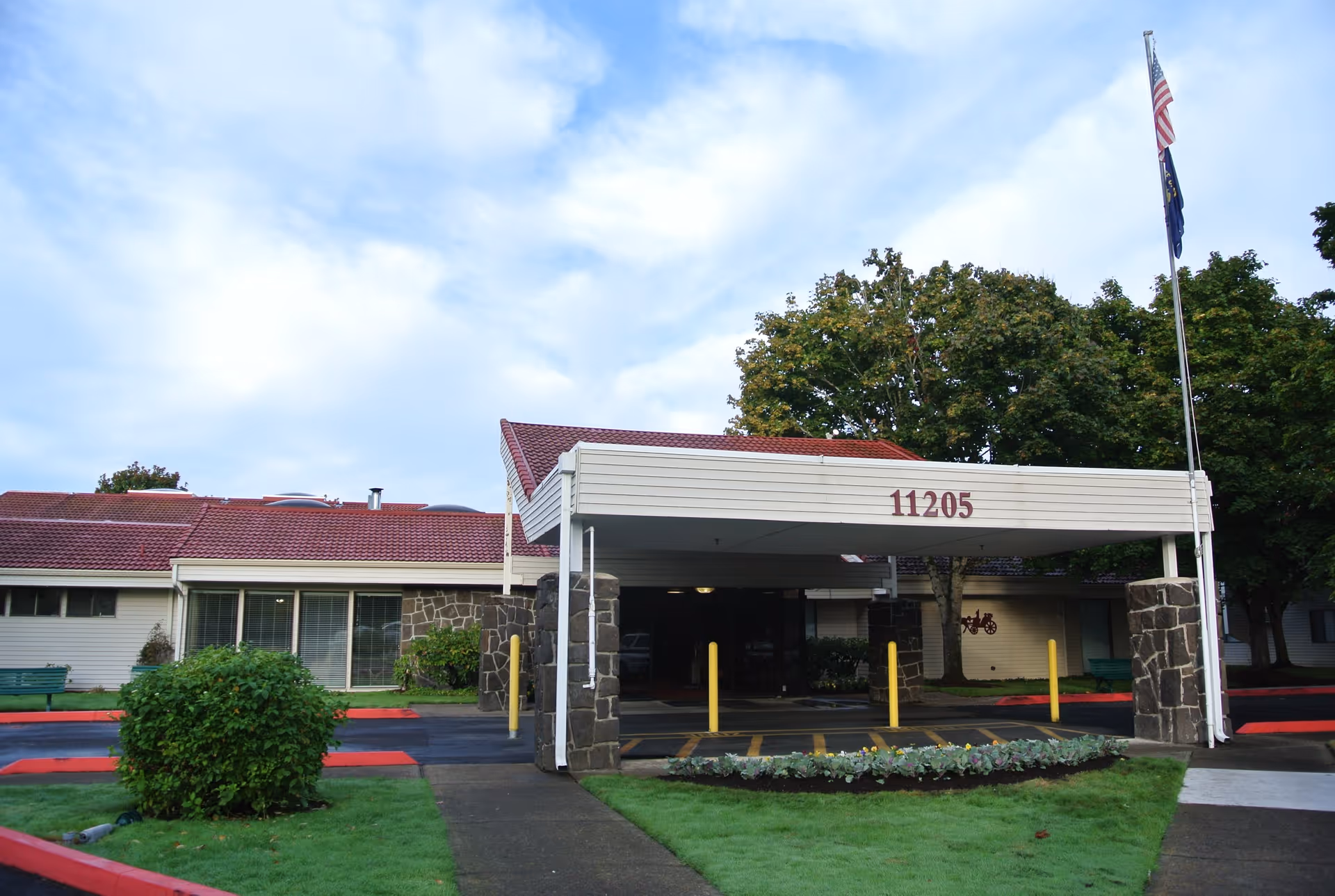 Exterior view of Summerfield Estates Retirement Community entrance with a covered drive and flagpoles.