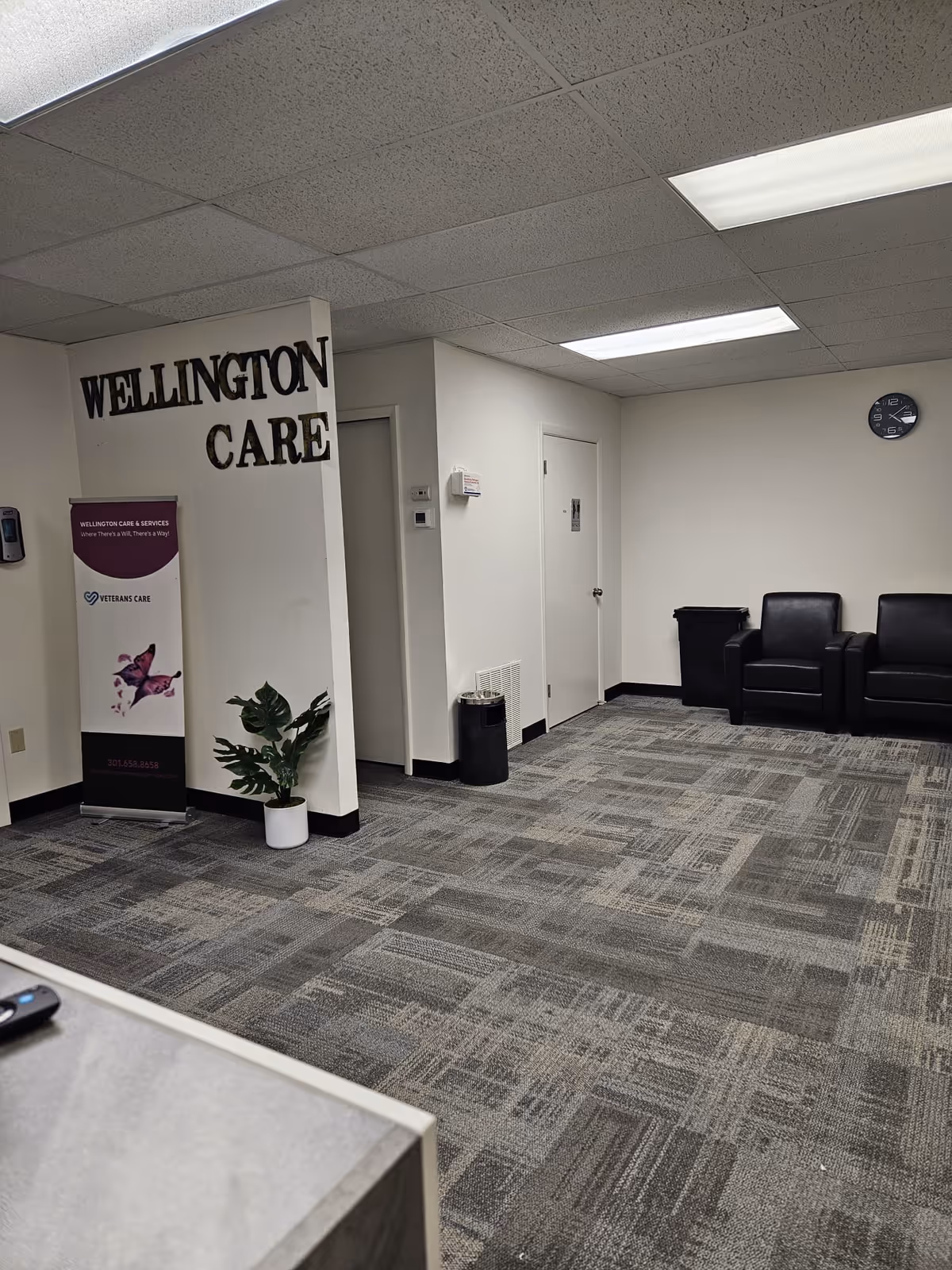 Interior lobby of Wellington Care & Services featuring seating, a sign, and a potted plant.