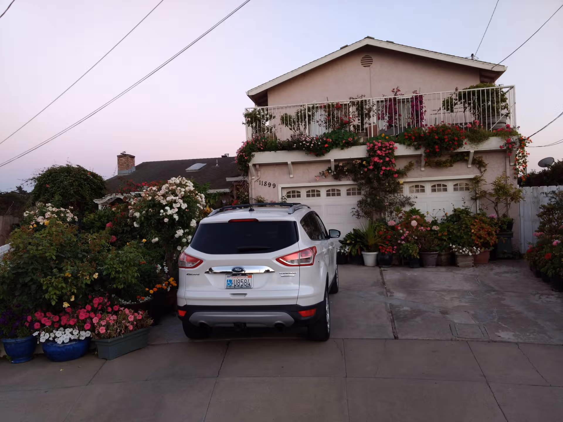 Front view of a two-story home with abundant flowers and a parked white SUV.