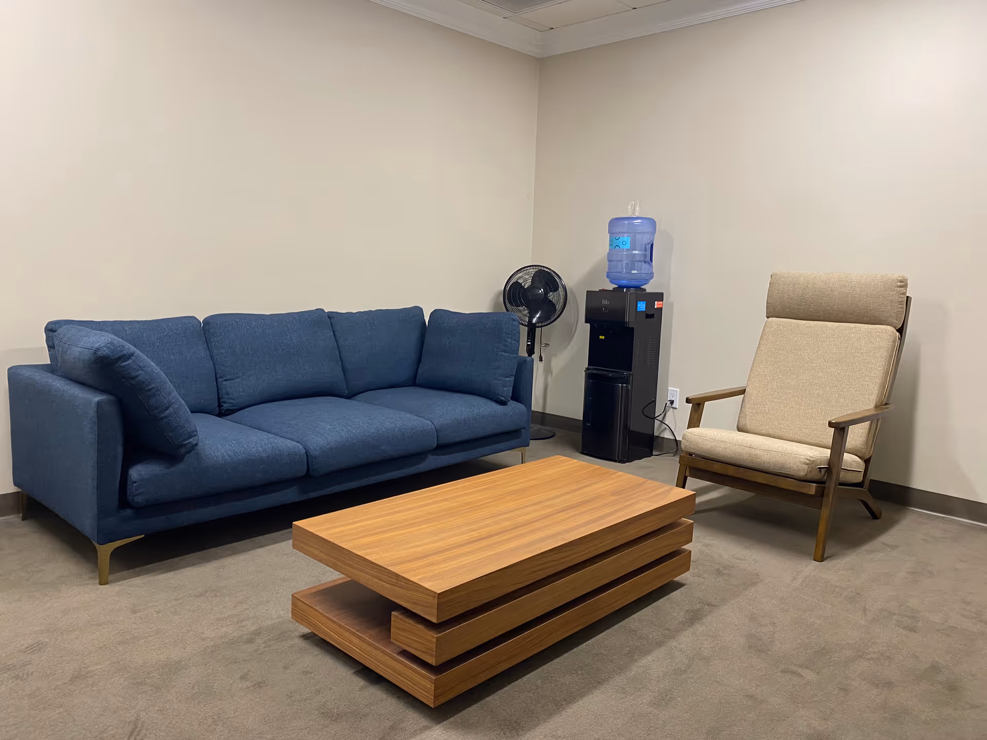 Cozy lounge area with blue sofa, beige armchair, coffee table, and water cooler.