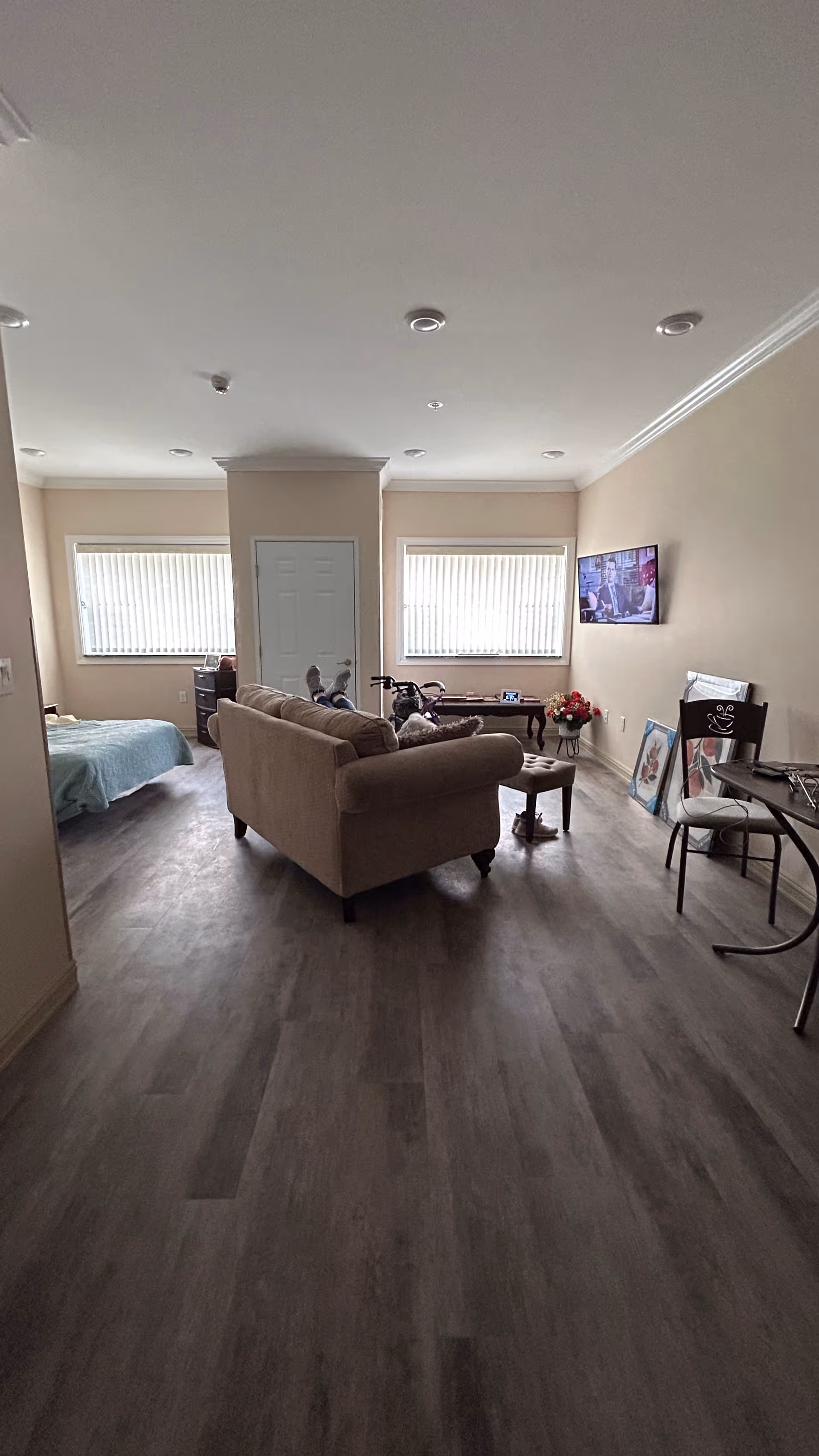 Living area with sofa, TV, windows, and a bed in the background.