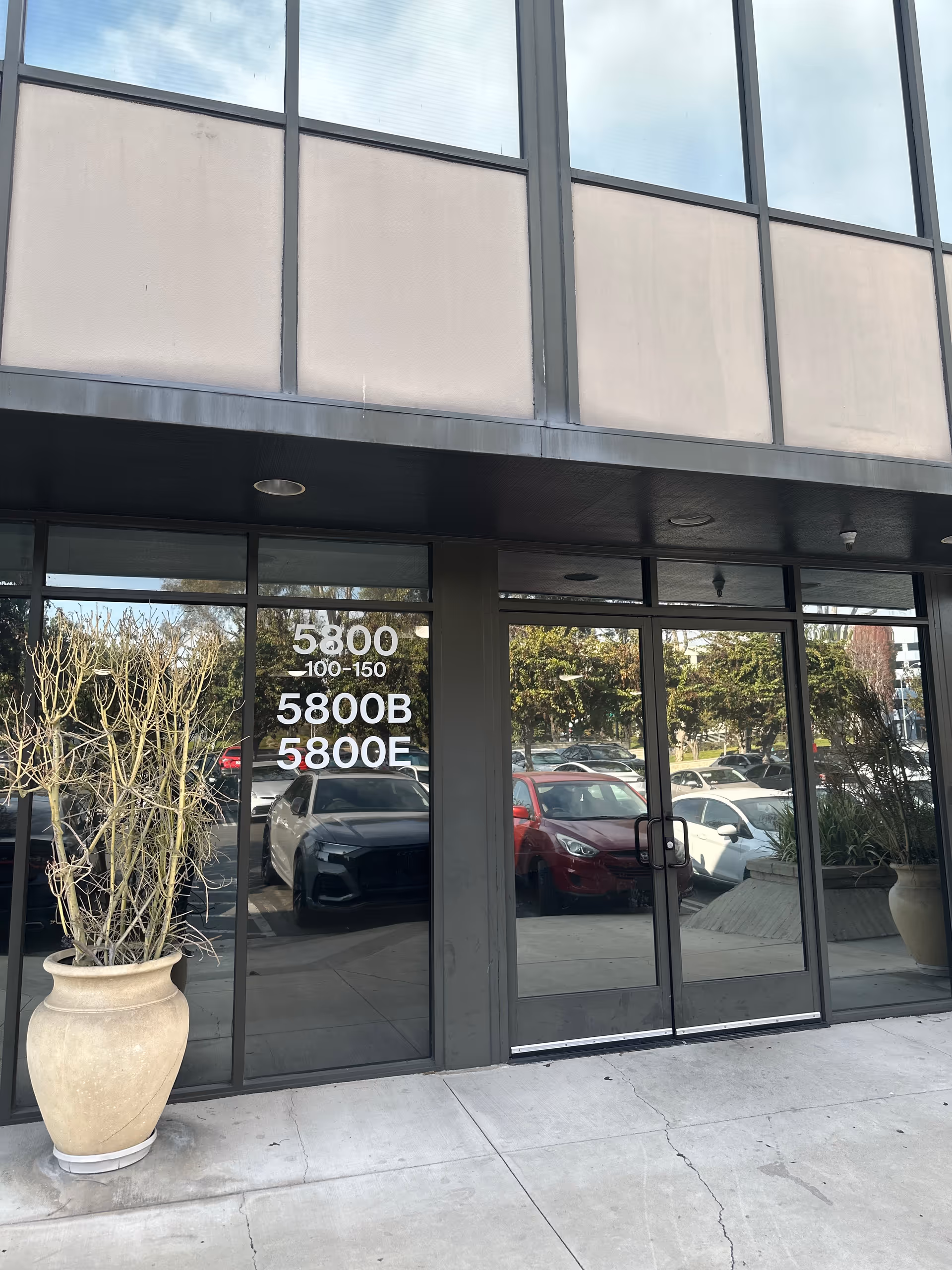 Glass storefront entrance with address numbers and potted plants outside.