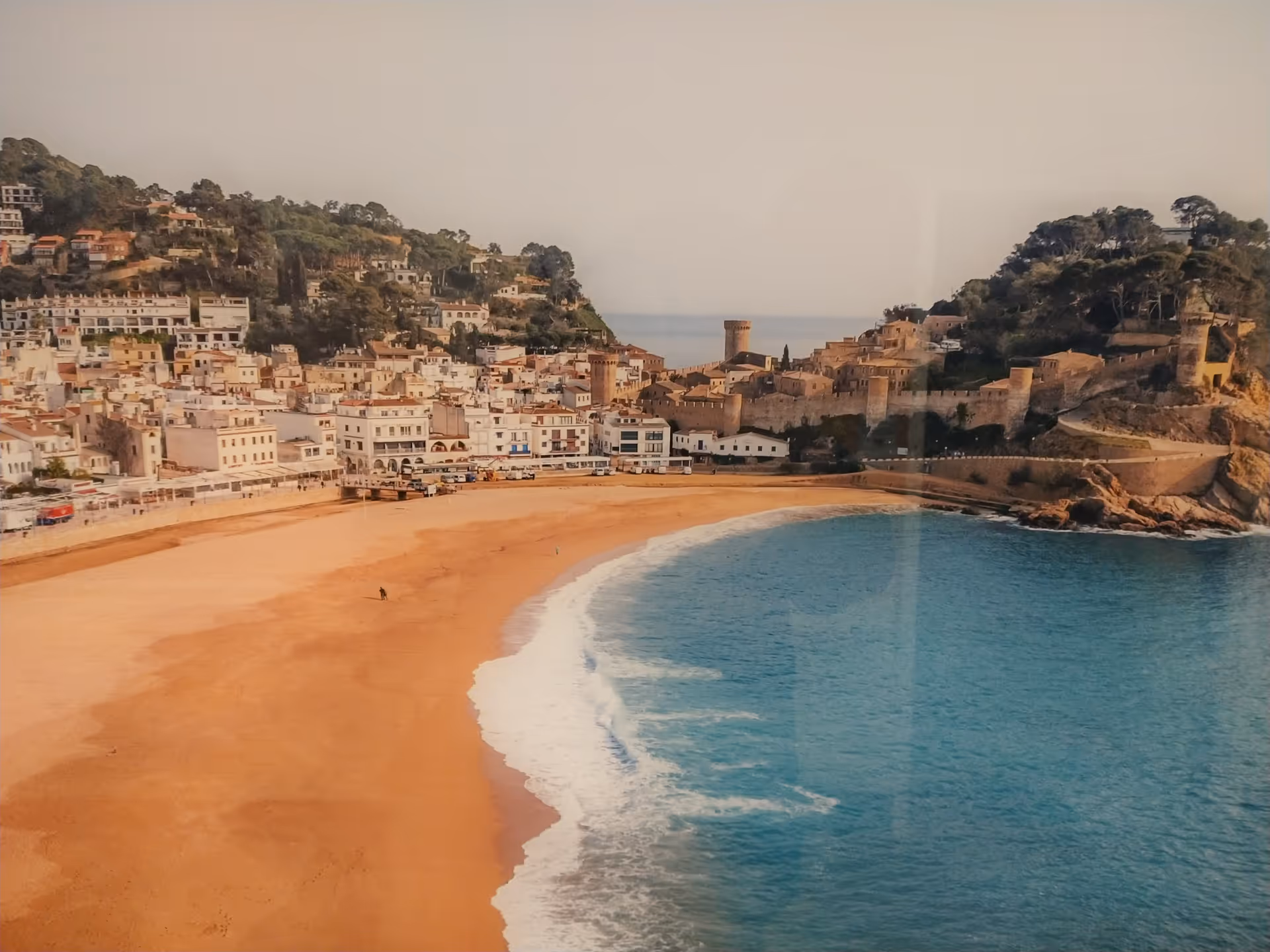 Coastal town, sandy beach, and blue sea viewed from a hillside overlook.