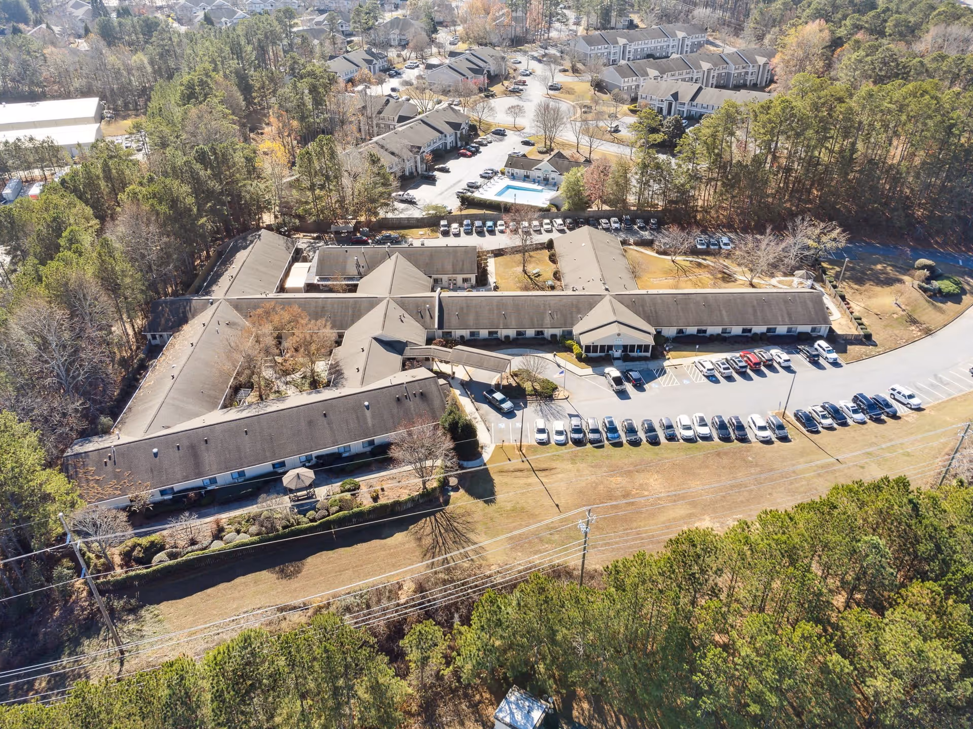 Aerial view of a single-story senior living facility complex with a parking lot and surrounding trees.