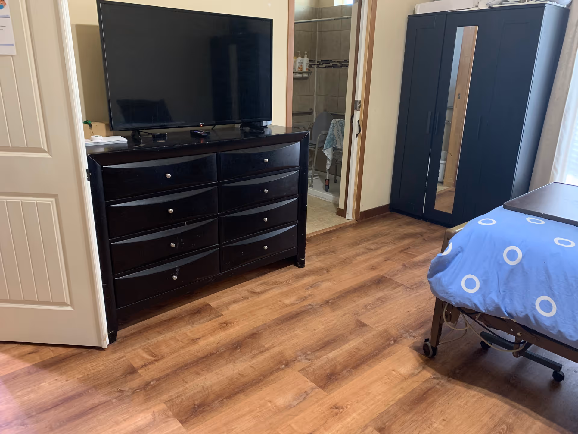 TV on a dark dresser beside a wardrobe and blue-covered bed in a furnished bedroom.