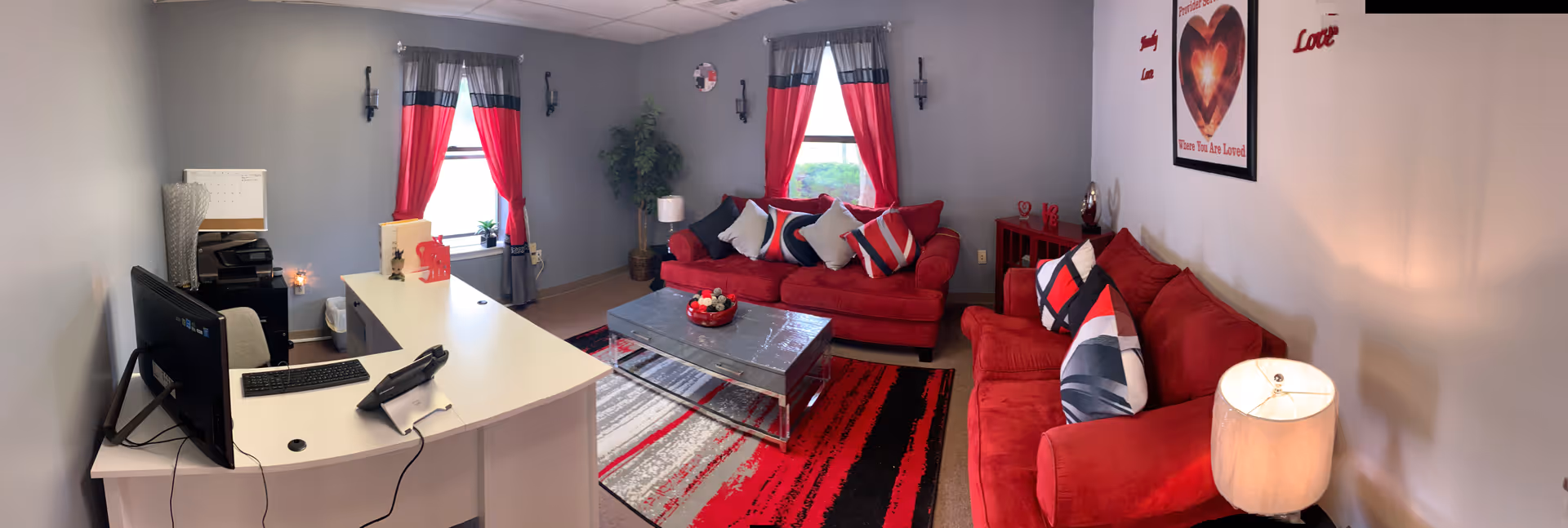 Bright living room with red couches, rug, and a desk computer setup.