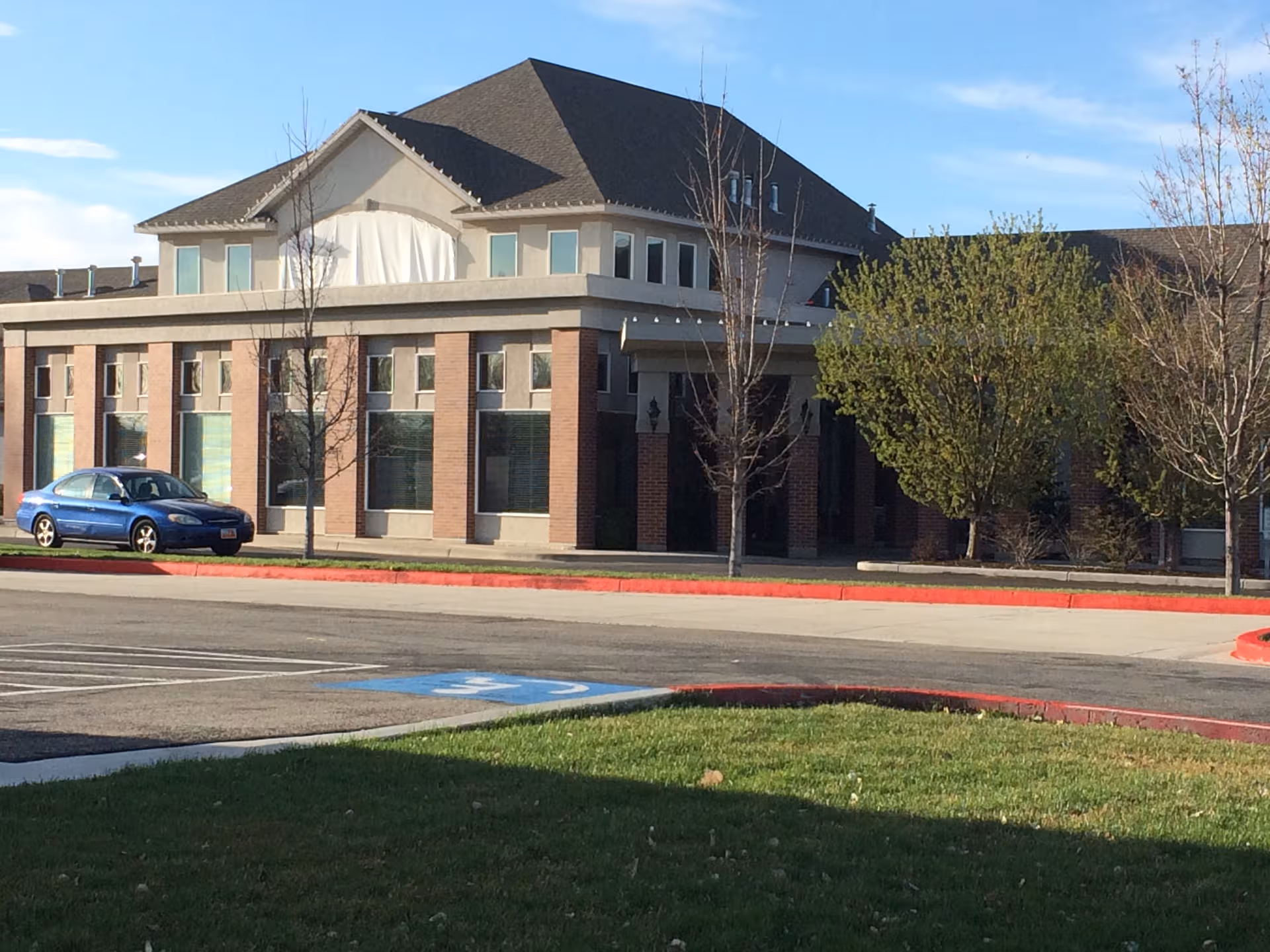 Exterior view of a brick senior living building with a blue car parked and trees.