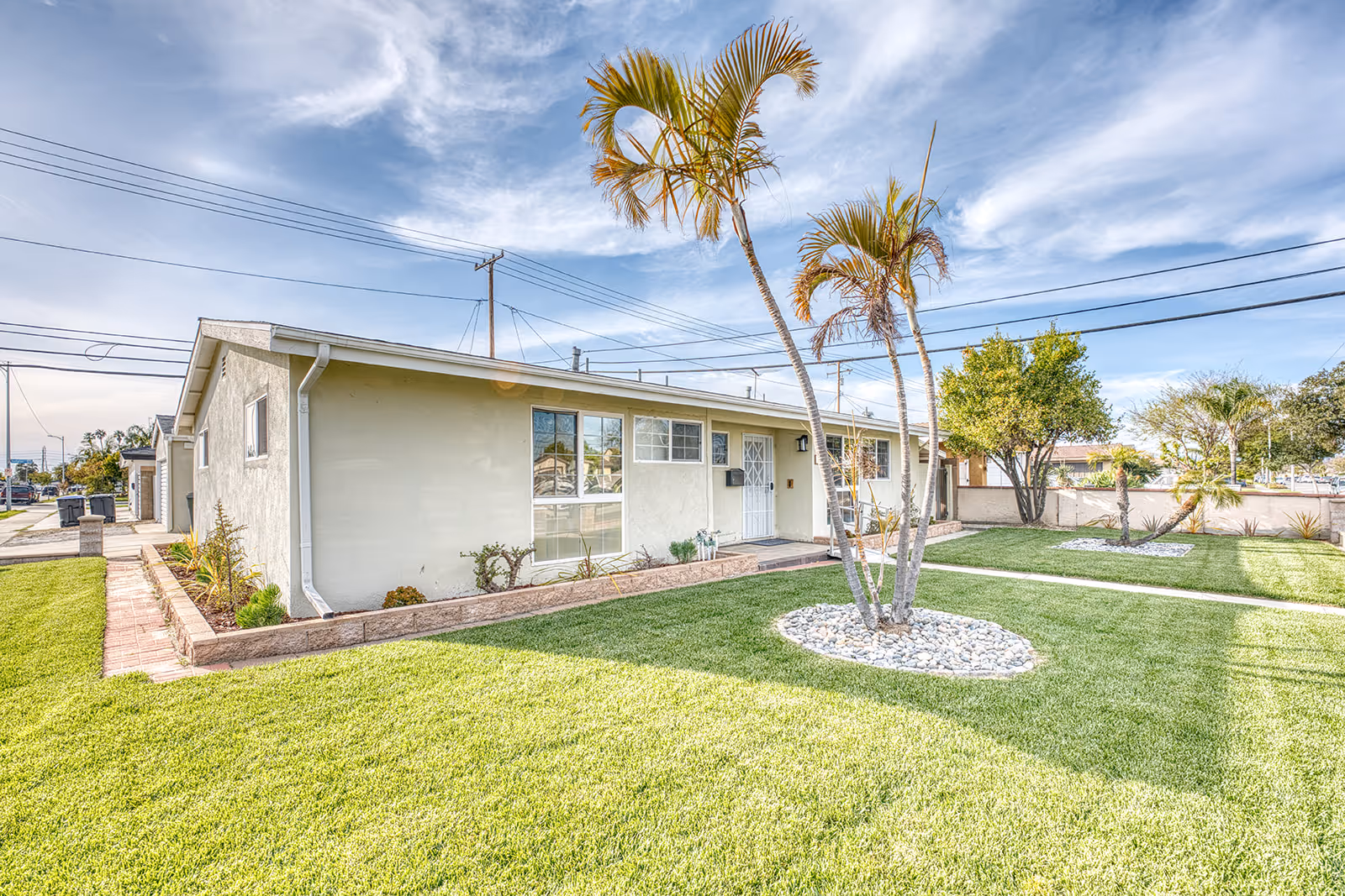 Exterior view of a single-story assisted living building with a manicured lawn and palm trees.