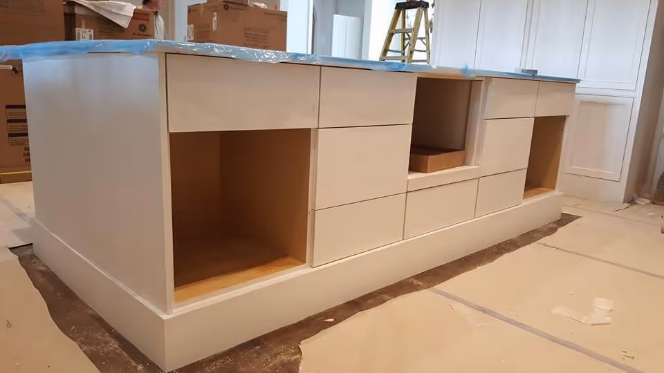 Under-construction kitchen island with white cabinetry, protective plastic, and scattered boxes.