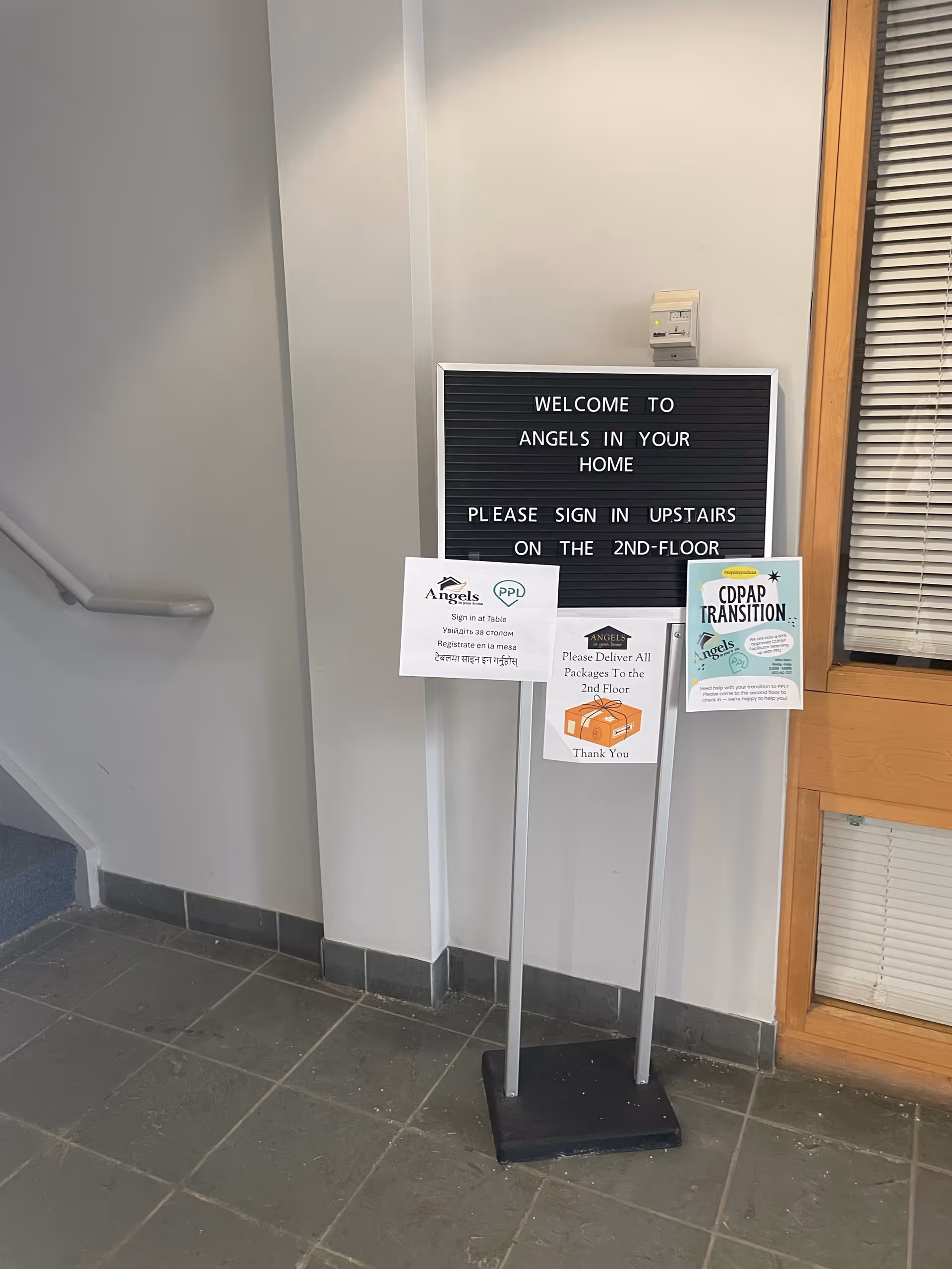Signboard in a hallway reads Welcome to Angels In Your Home with posted notices.