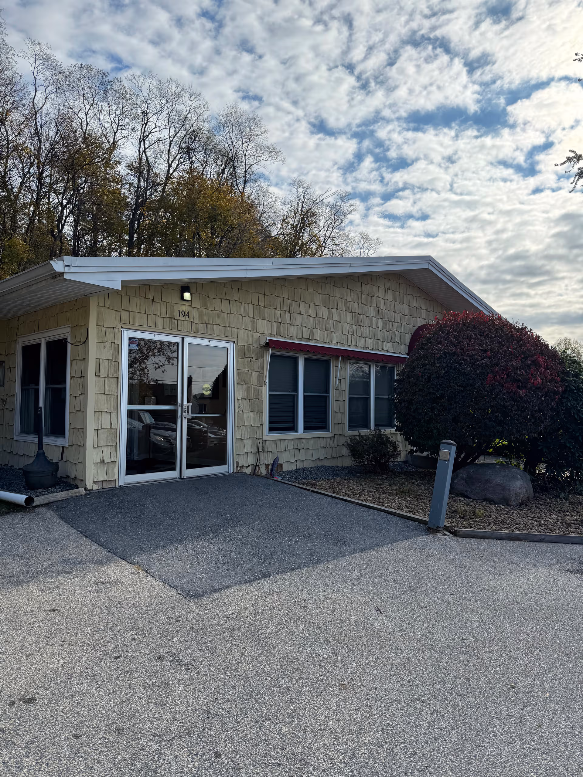 Front exterior of a beige nursing home with glass entrance and surrounding shrubbery.