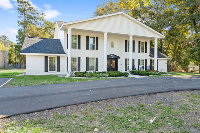Front view of a white two-story senior care home with columns and landscaping.