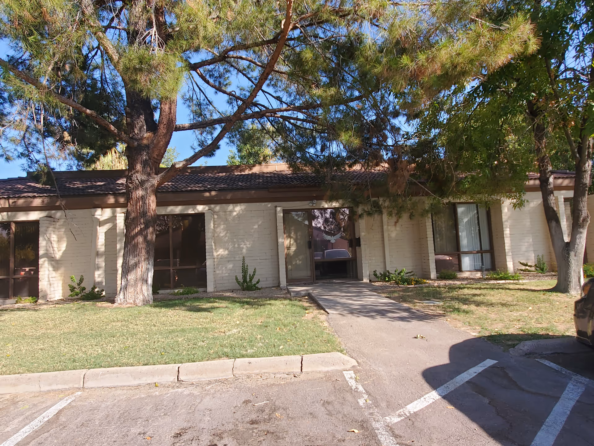 Exterior view of a single-story senior living facility with trees and a driveway.