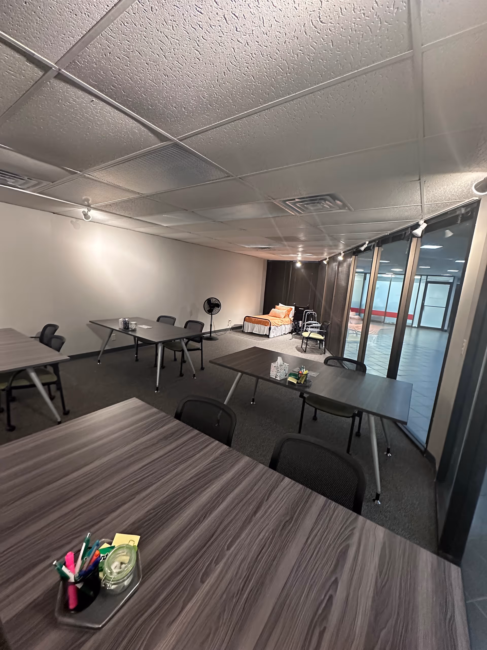 Interior multipurpose room with tables, chairs, and a bed in the back.