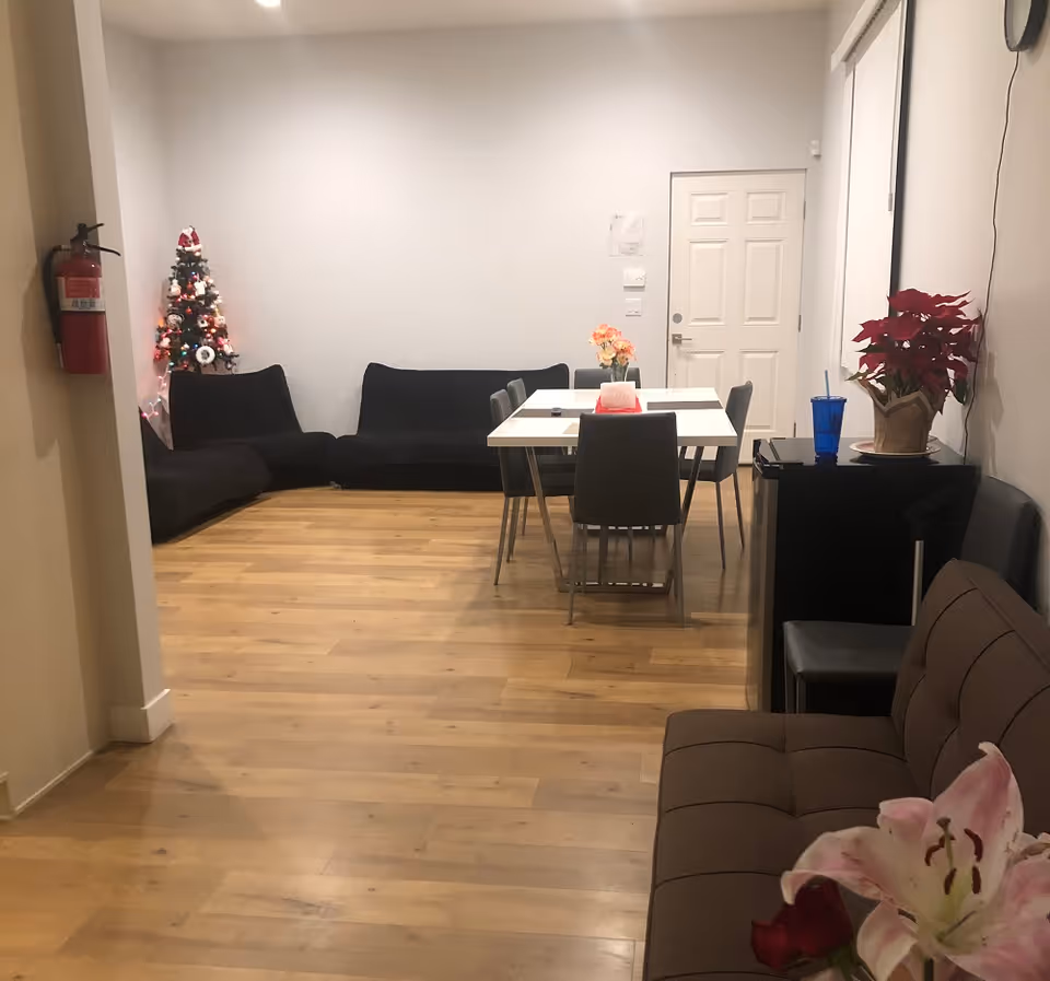 A furnished senior living lounge with a dining table, couches, holiday decor, and plants.