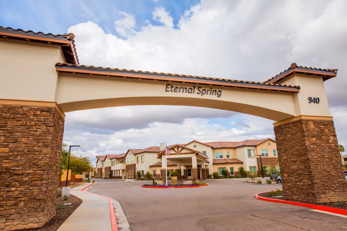 Arched stone entrance reading "Eternal Spring" over a driveway leading to a multi-story senior living building.