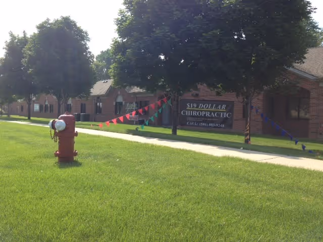 Exterior shot of a brick building with a $19 Chiropractic banner along the lawn and sidewalk.