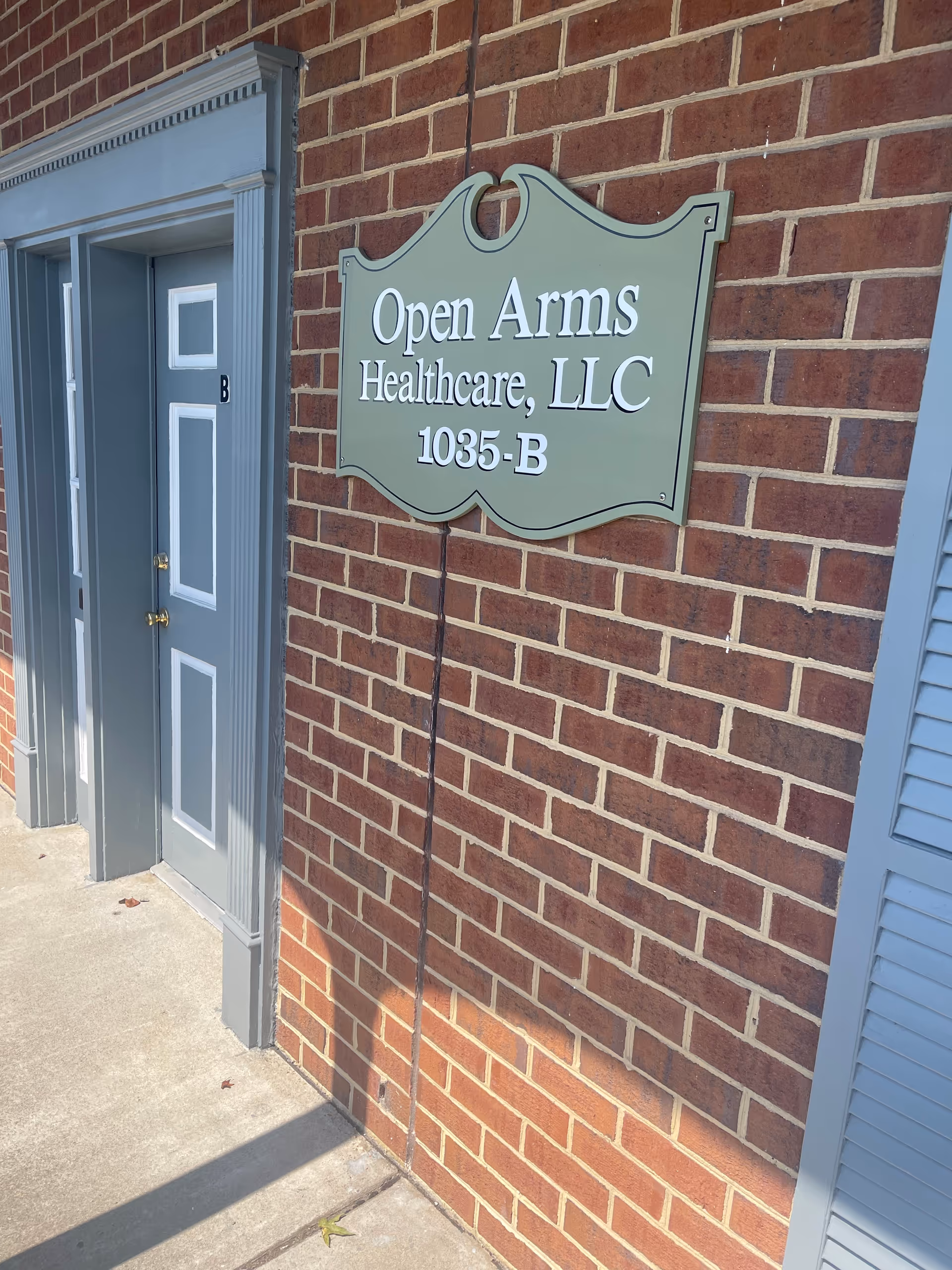Brick exterior with a blue door and an Open Arms Healthcare sign.