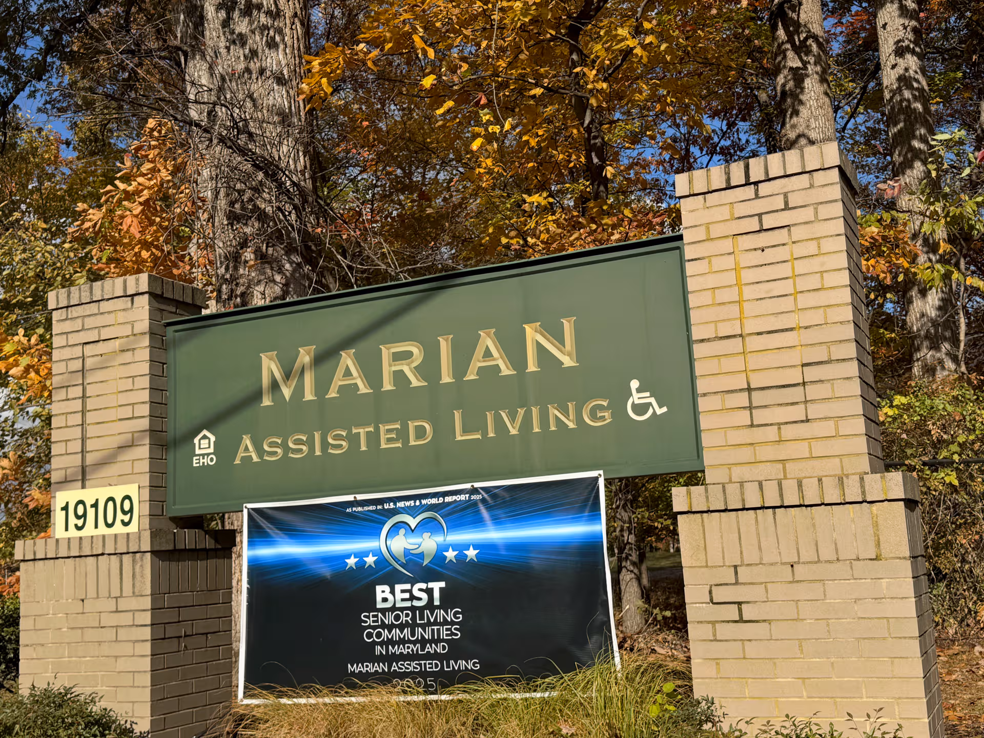 Green Marian Assisted Living sign framed by brick pillars and autumn trees.
