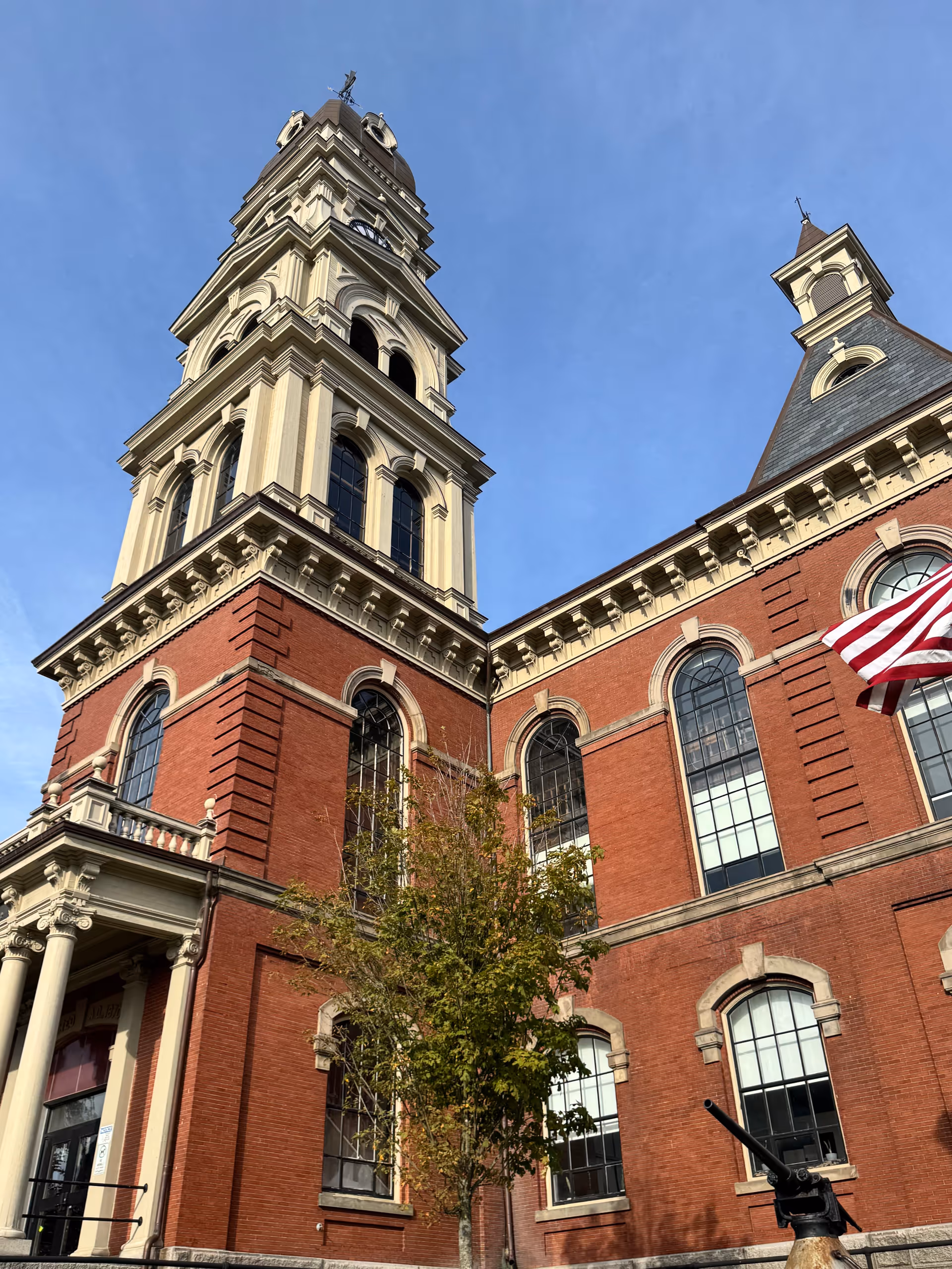 Tall brick building with a clock tower and American flag under a clear blue sky.