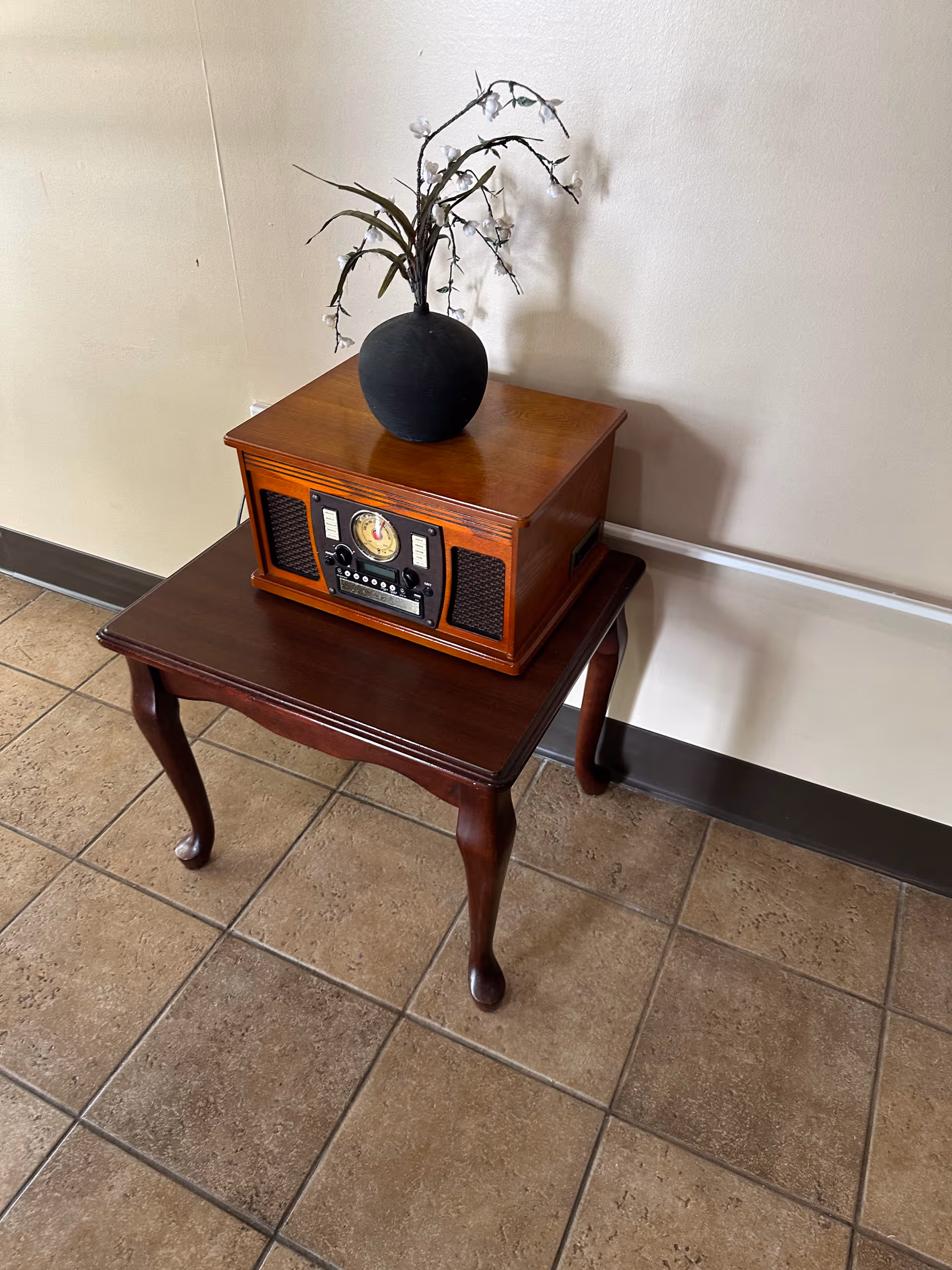Two-tier wooden tables support a vintage radio and a black vase with white branches.