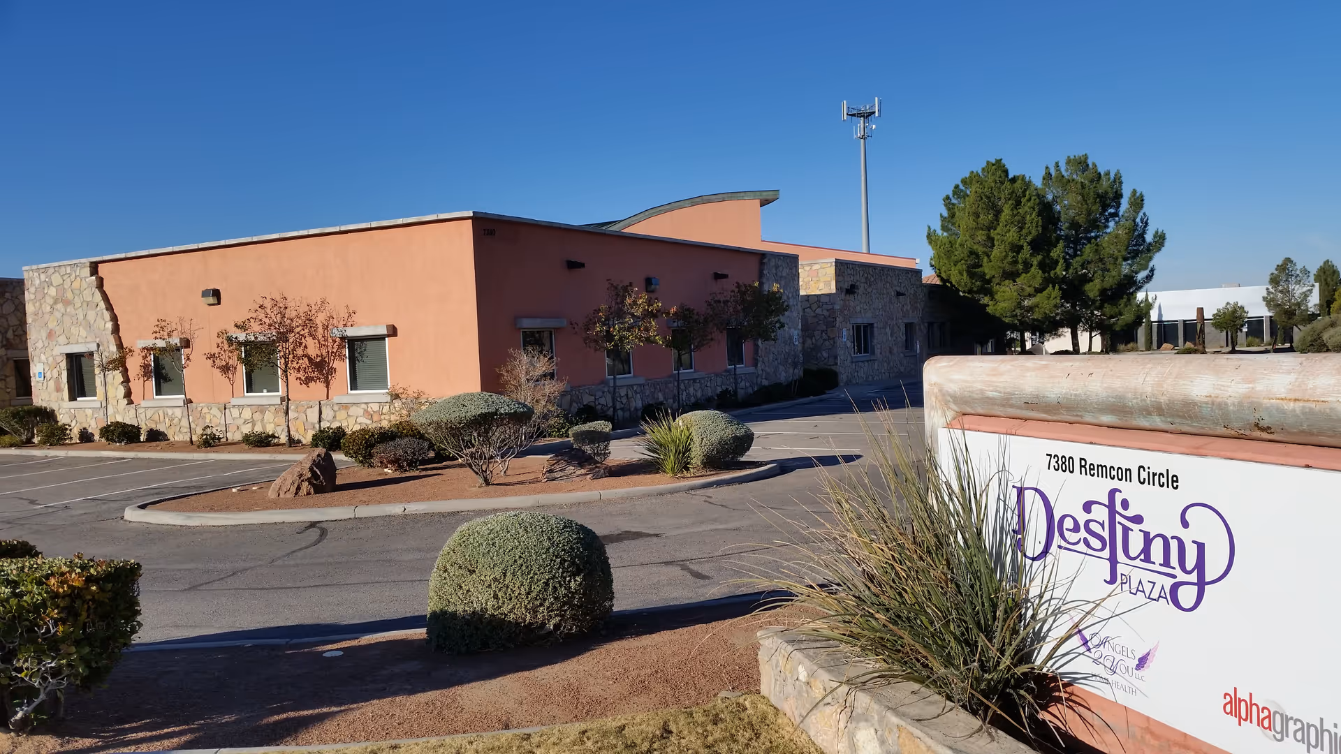 Exterior view of a peach-colored, single-story senior living facility with a sign and desert landscaping.