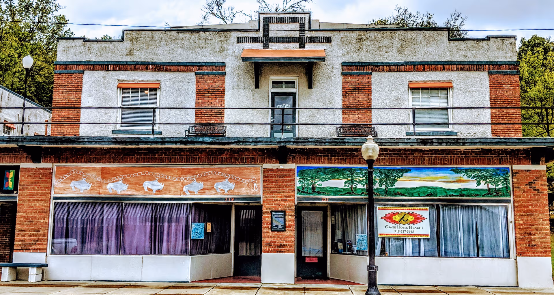 Brick storefront building with murals, Osage Nation Home Health sign, and a streetlamp on the sidewalk.