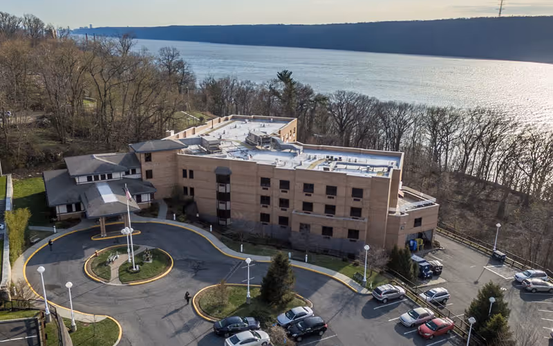 Aerial view of a brick senior living facility with circular driveway along a river.