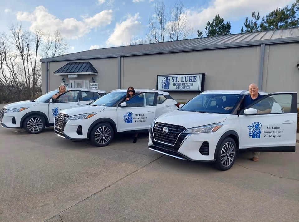 Three white St. Luke Home Health & Hospice vehicles parked outside the facility.