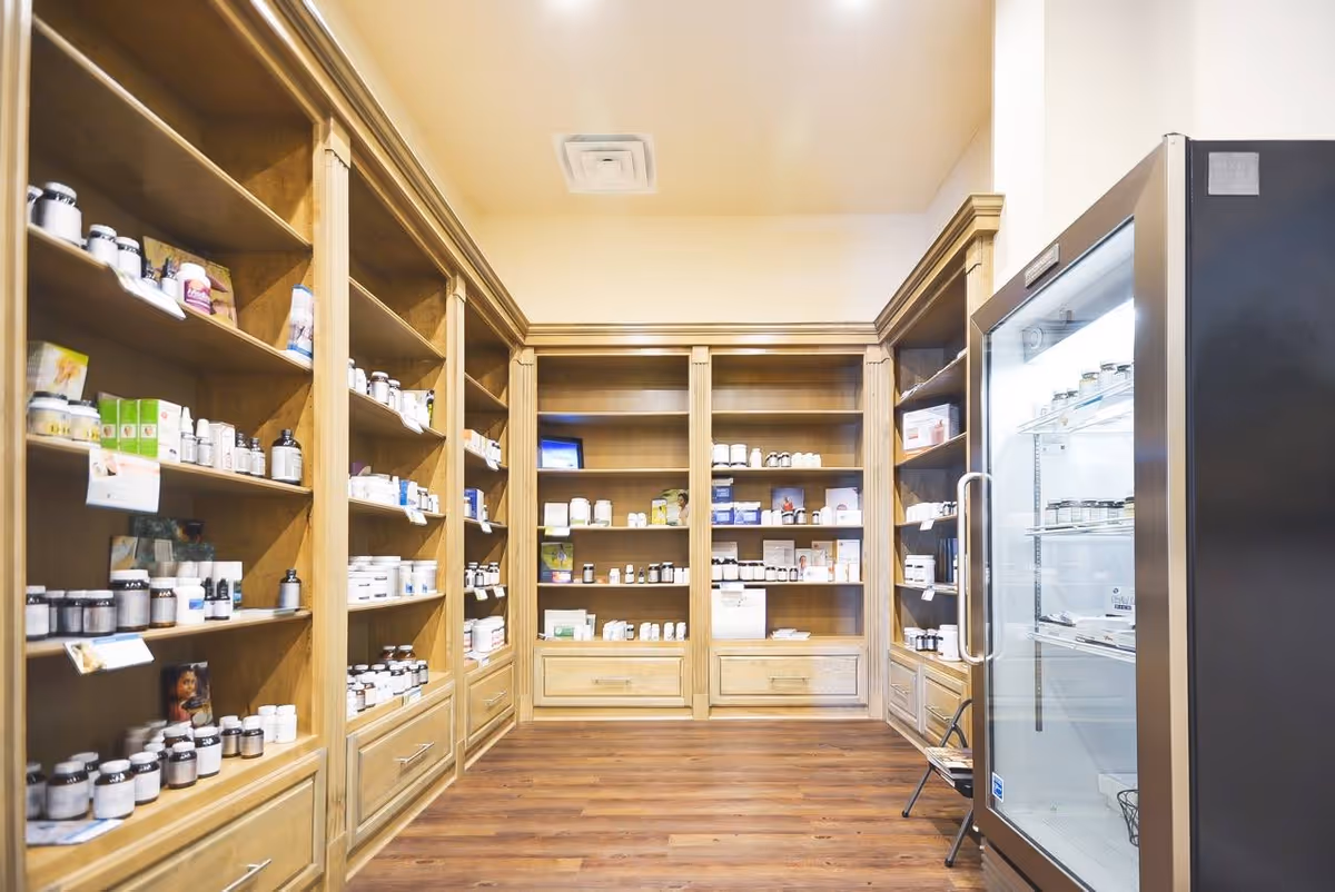 Interior medical supply room with wooden shelves full of bottles and a glass-door refrigerator.