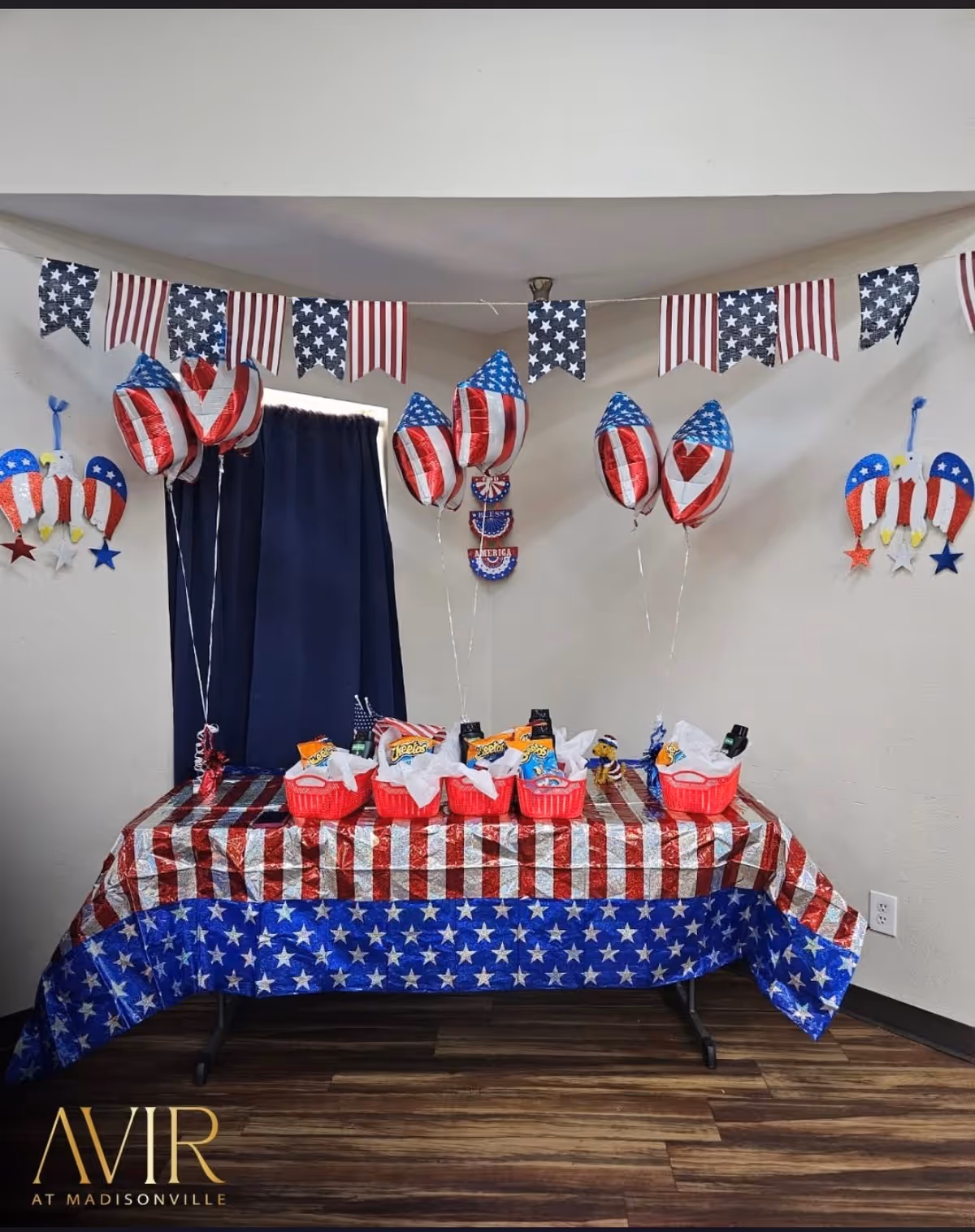 Patriotic indoor table setup with red-white-blue tablecloth, balloons, and candy baskets.