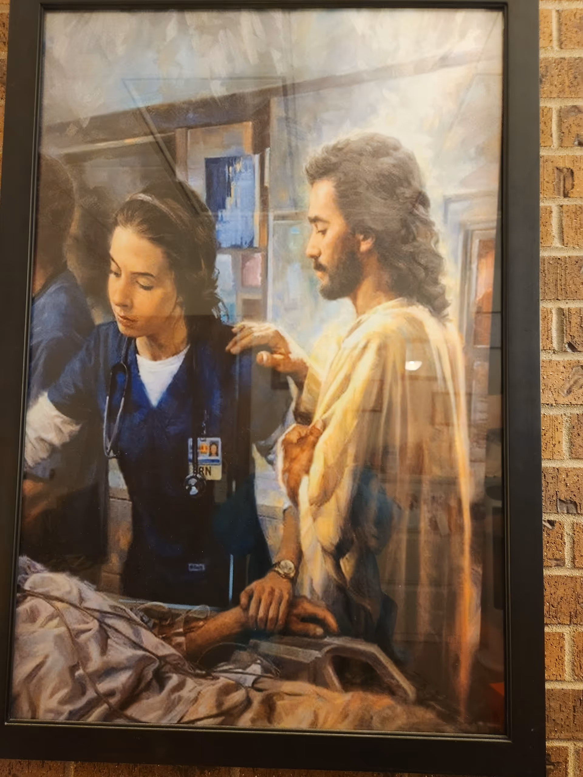 Framed painting of a nurse with a patient in a hospital scene on a brick wall.