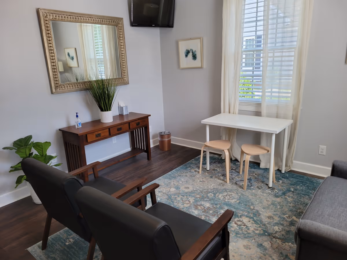 Cozy senior living lounge with black chairs, a console table, mirror, planters, and a white table.