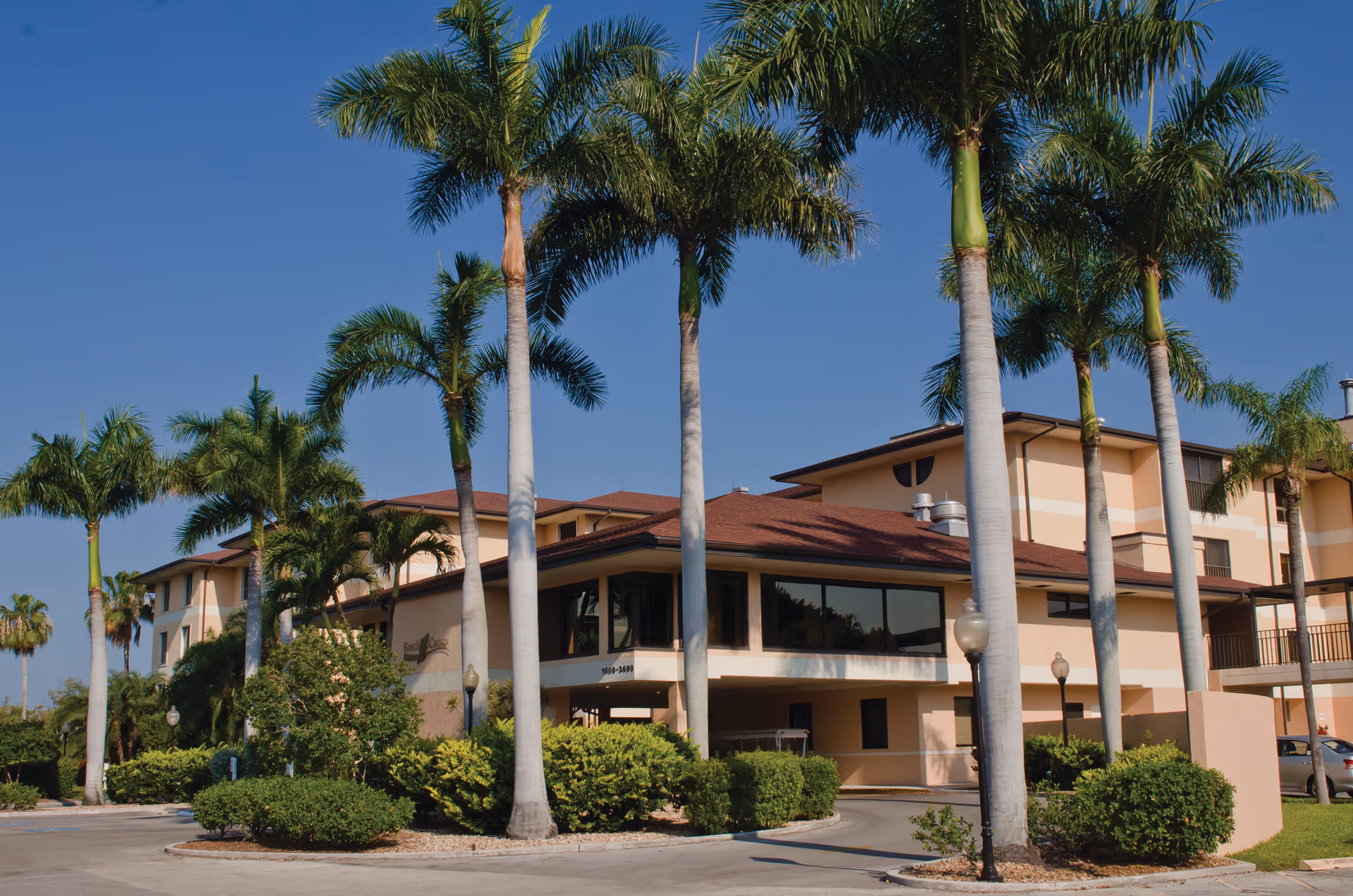 Exterior view of King's Crown at Shell Point senior living facility with palm trees, shrubs, and a clear blue sky.