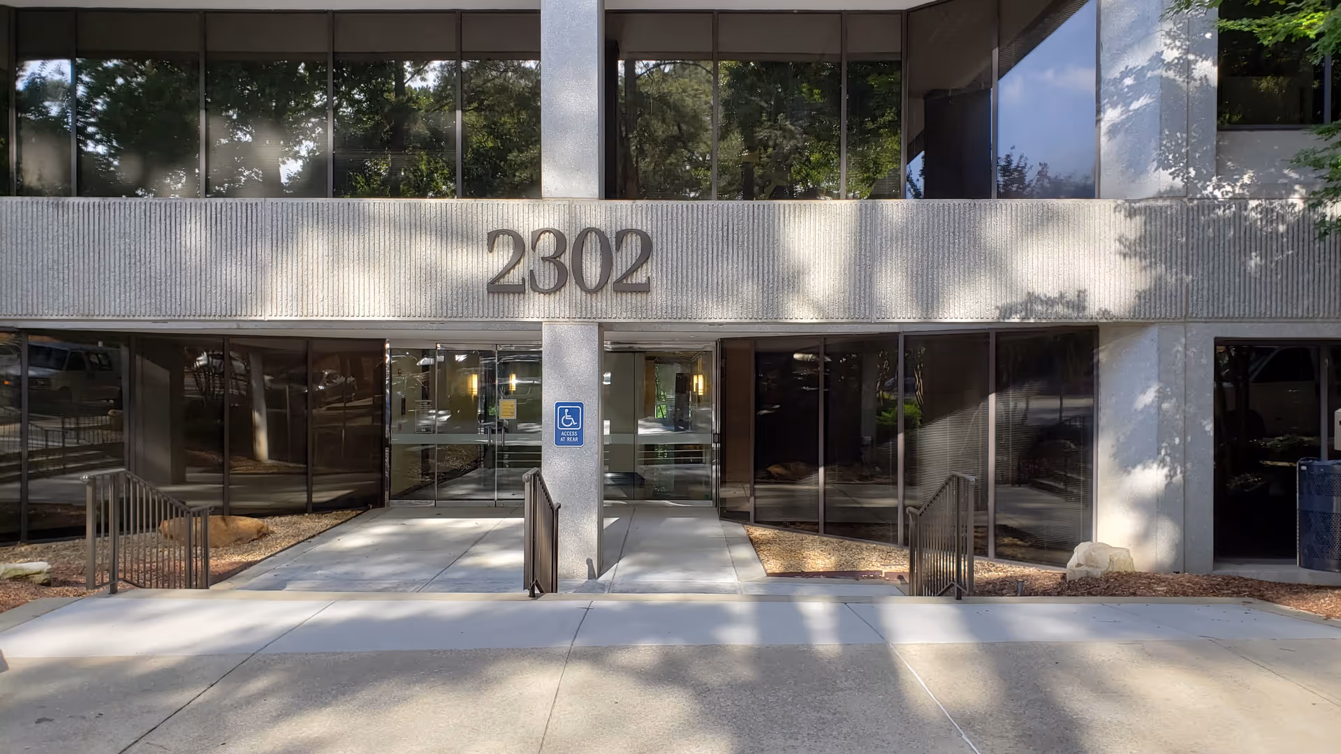 Front entrance of a modern building with large glass doors and a wheelchair ramp.