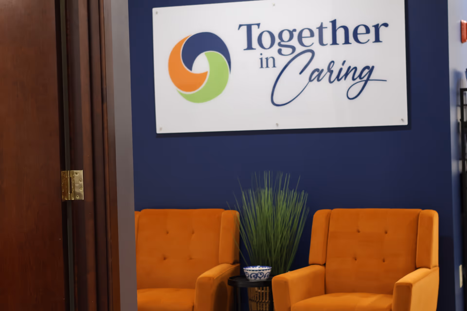 Lobby area with orange chairs, blue wall, and a sign reading Together in Caring Albany