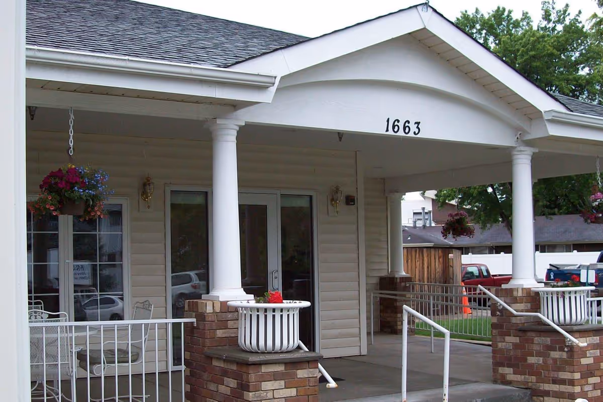 Front entrance of a memory care facility with white columns, hanging baskets, and porch seating.