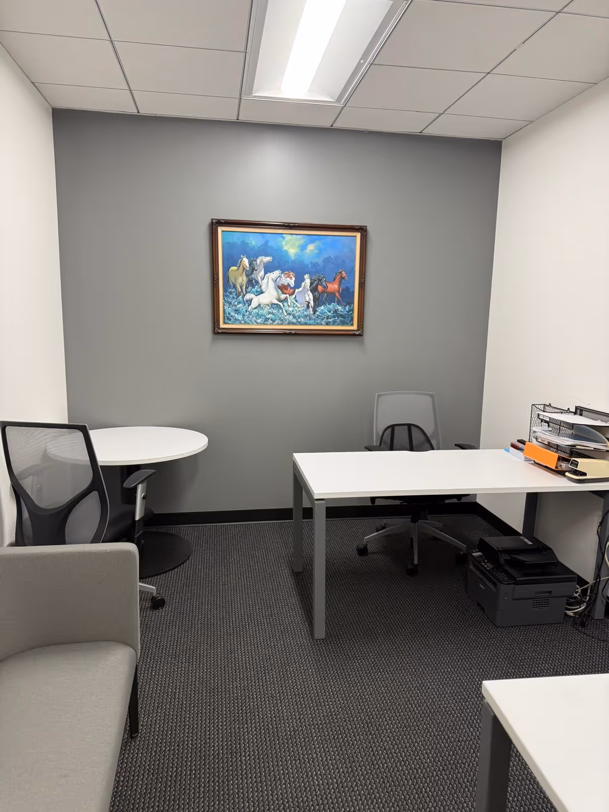 Small office area inside GiveNCare In-Home Care Corporation facility with desk, chairs, printer, painting.