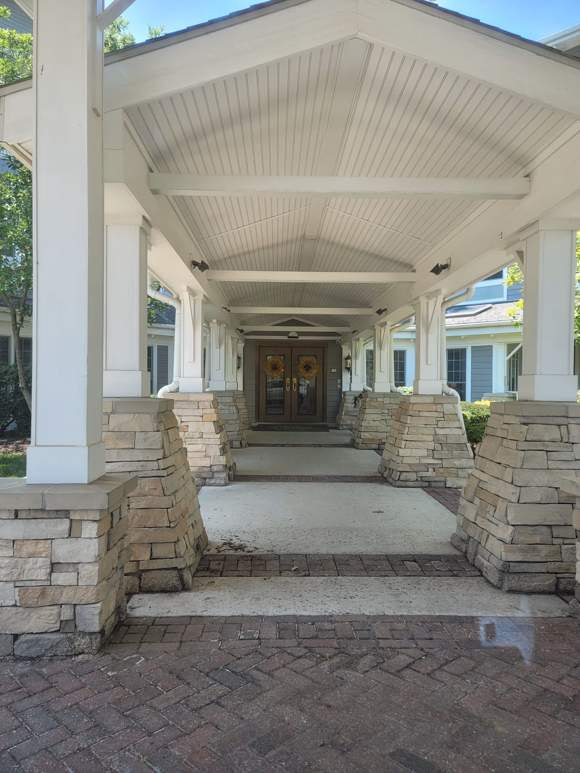 Covered walkway with stone pillars leading to double doors at a building entrance.