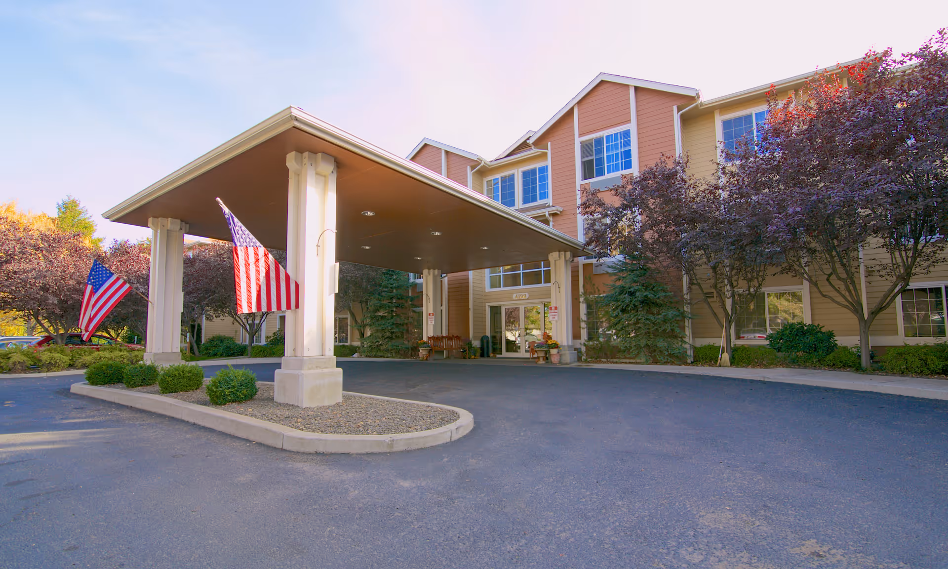 Exterior of Brookdale Yakima with a porte-cochère entrance, flags, and landscaped driveway.