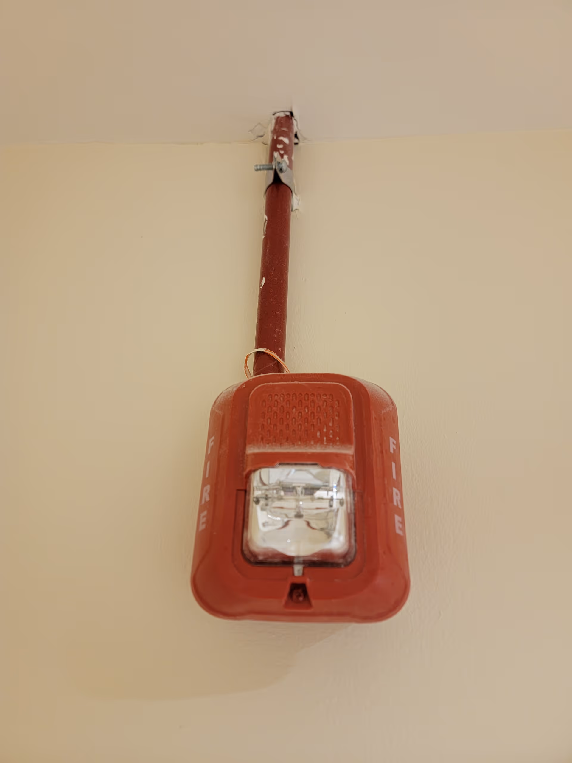 Red fire alarm pull station mounted on a cream interior wall with conduit.