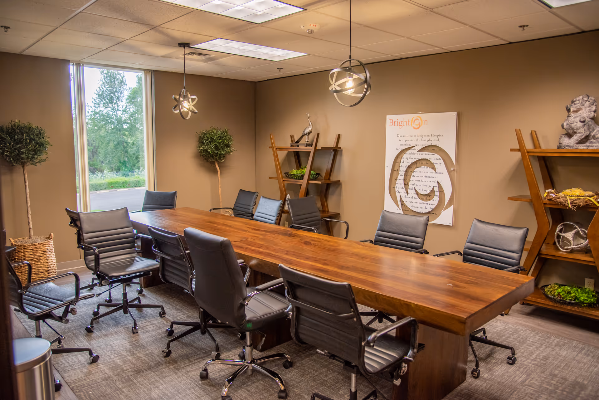 A modern conference room with a long wooden table, black chairs, and decorative shelves.