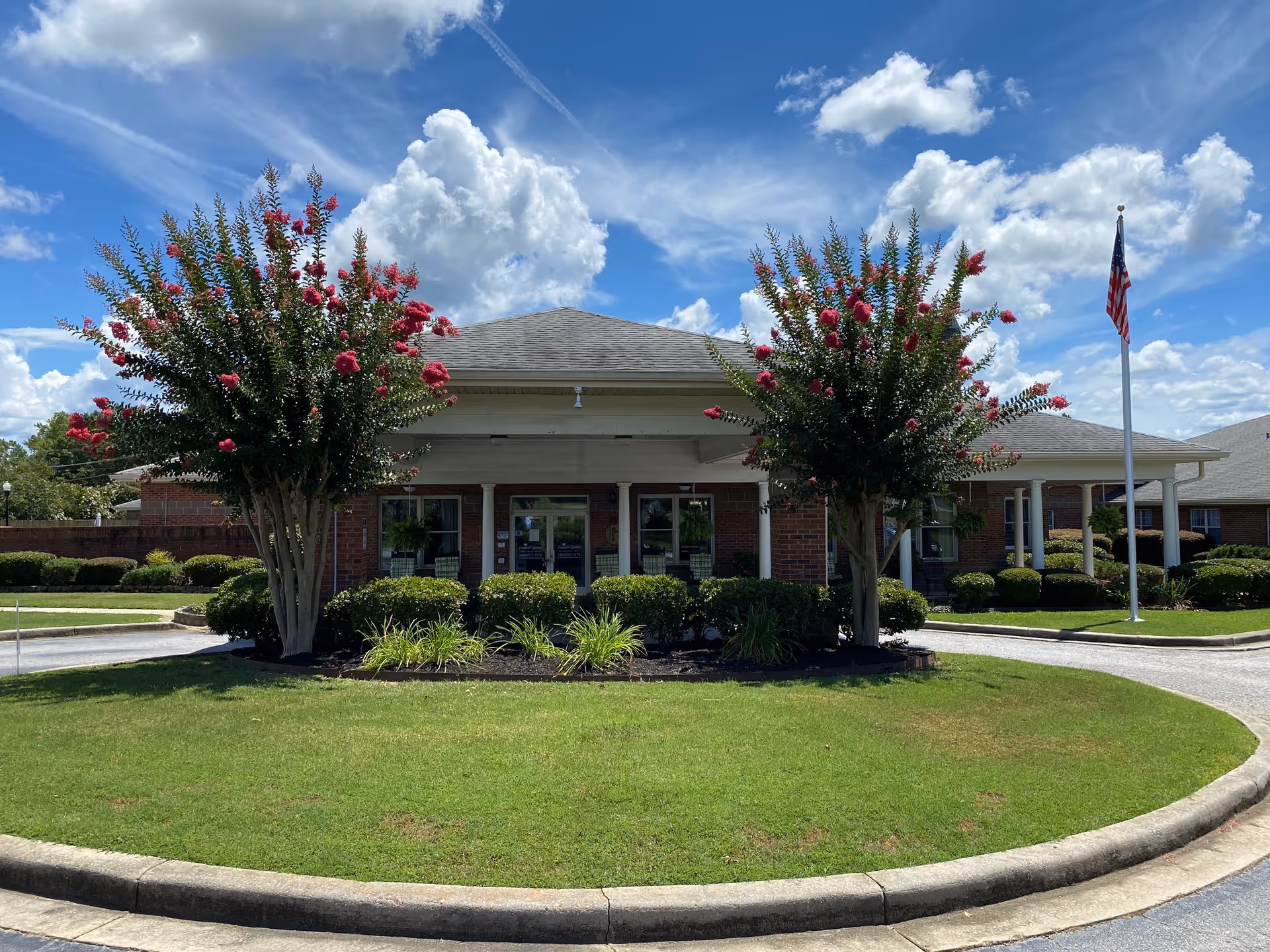 Emerald Gardens exterior: brick senior living facility with circular driveway, manicured landscaping, and flagpole.