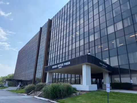 Exterior view of a tall glass office building with a covered entrance and landscaping.